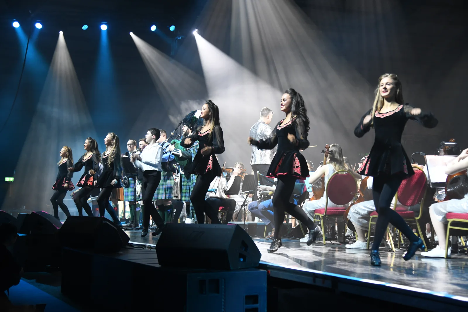 Irish dancers performing on a lit stage with musicians behind them
