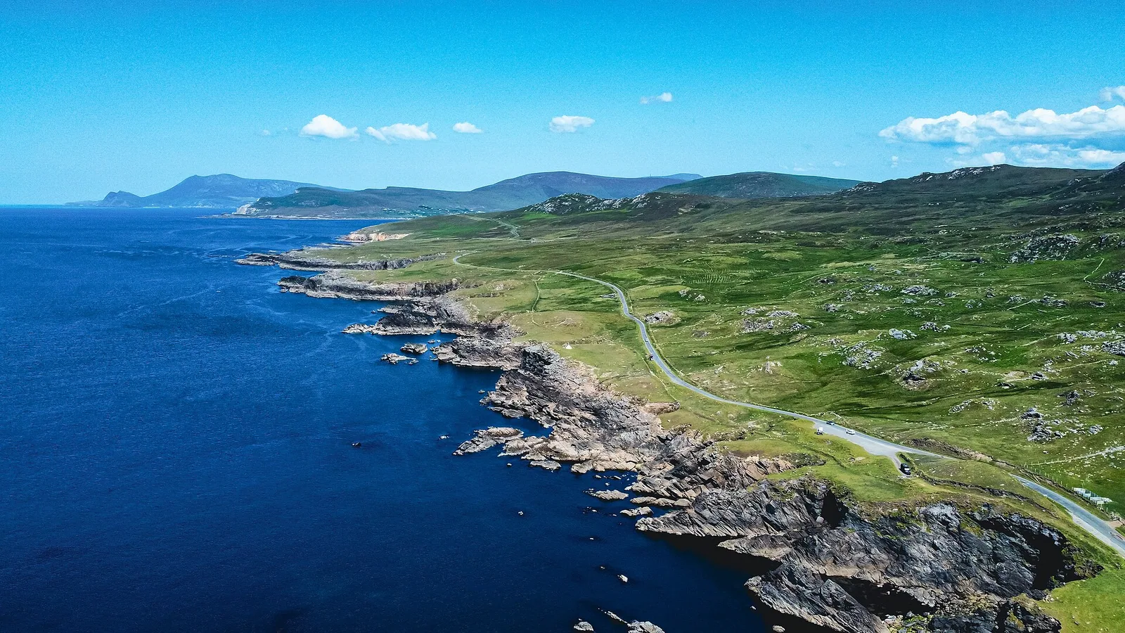 An aerial view of Achill Island’s green cliffs, winding coast road and deep-blue Atlantic Ocean.